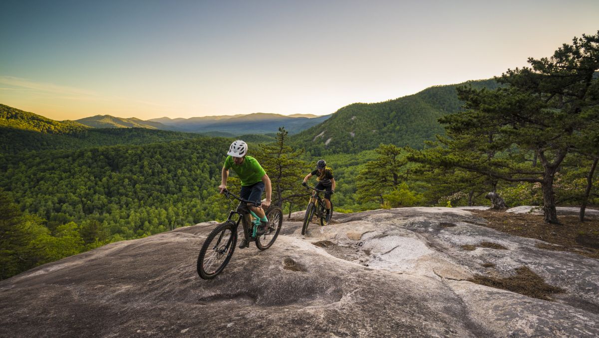Two cyclists biking up stone mountain with green mountains in background