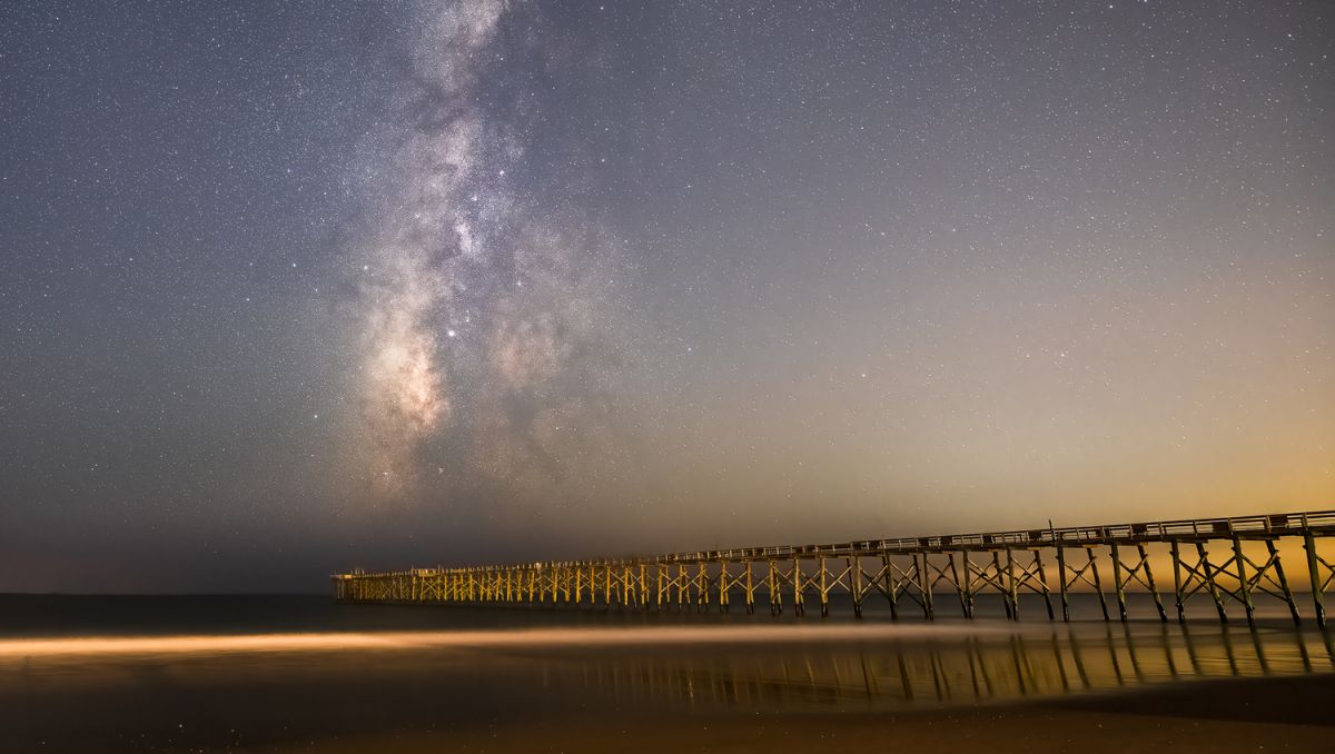 Pier jutting out into ocean at night with Milky Way and stars shinning in sky