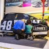 white man and middle-school-age black girl change tire on stock car at NASCAR Hall of Fame Pit Crew Practice exhibit