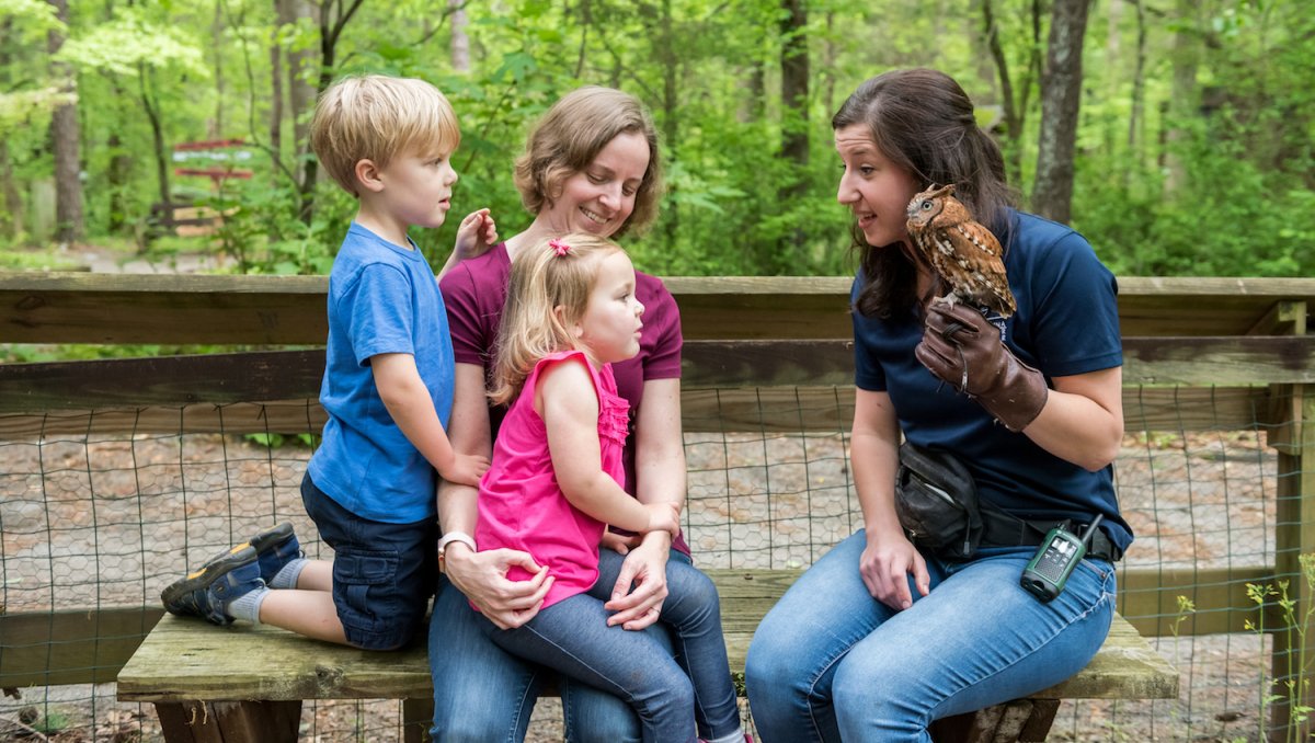 Woman holding owl sitting next to family, teaching about birds