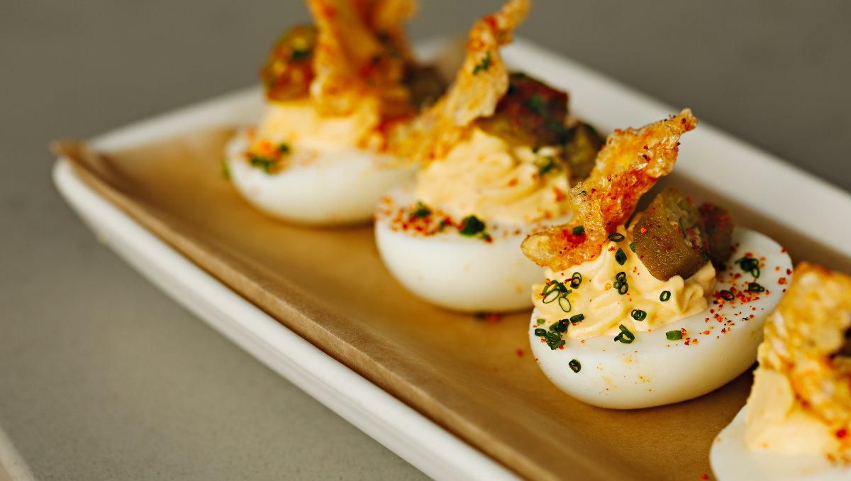 Four fancy deviled eggs on wood and white glass platter