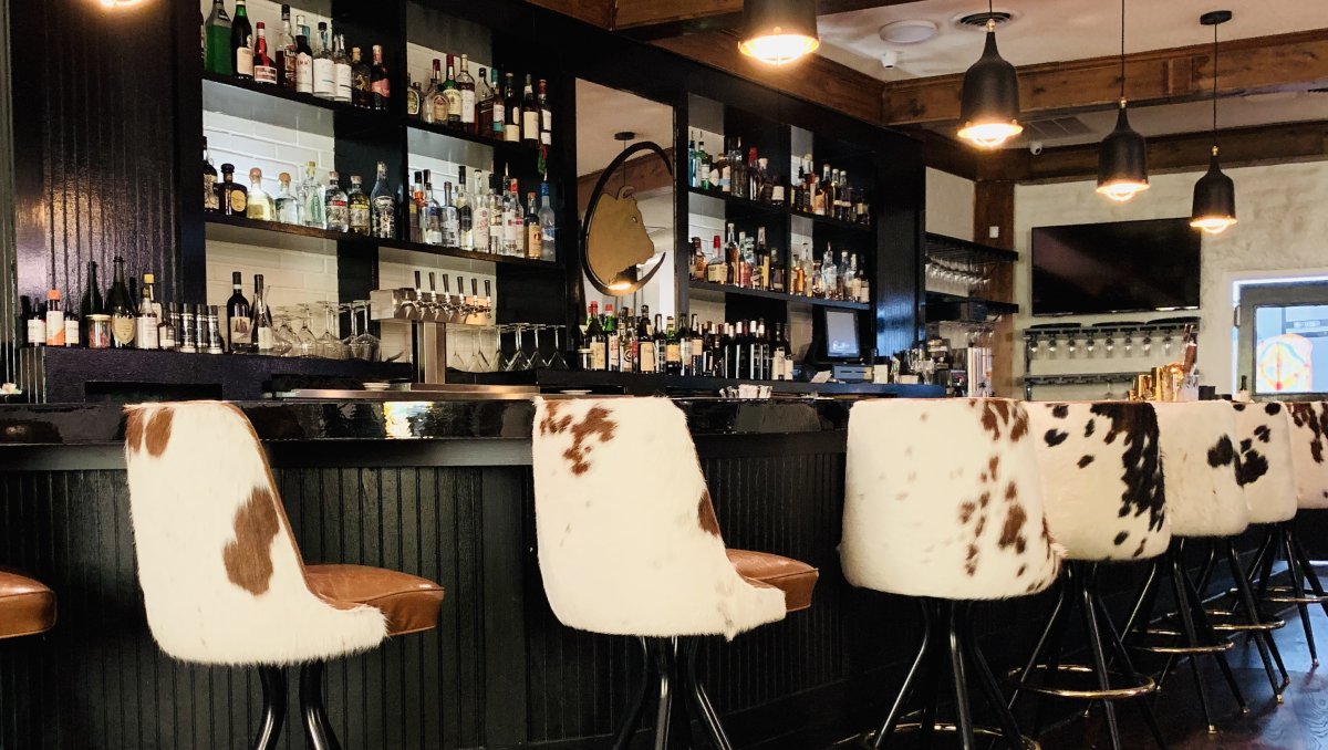 Cow-hide stools sitting at black bar inside steakhouse