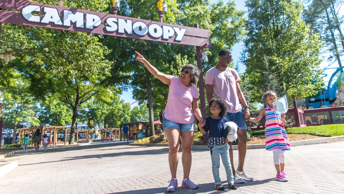 Family of four happily standing outside Camp Snoopy at Carowinds during daytime.