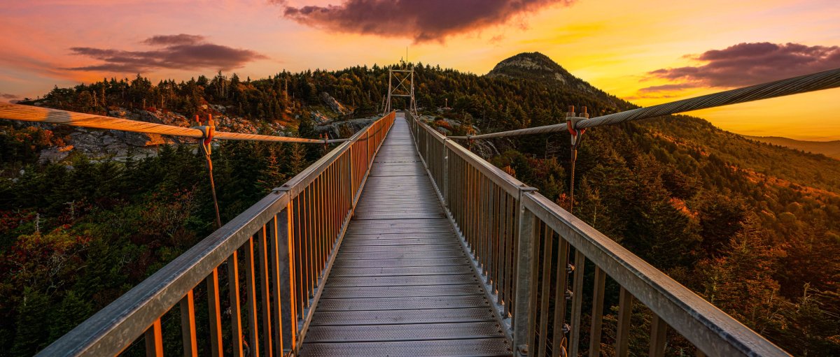 Mile High Swinging Bridge walkway surrounded by fall foliage and brilliant pink sky