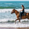 Woman riding horse in ocean waves during daytime.