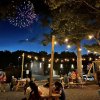 People eating ice cream at picnic tables at night with fireworks on display in background