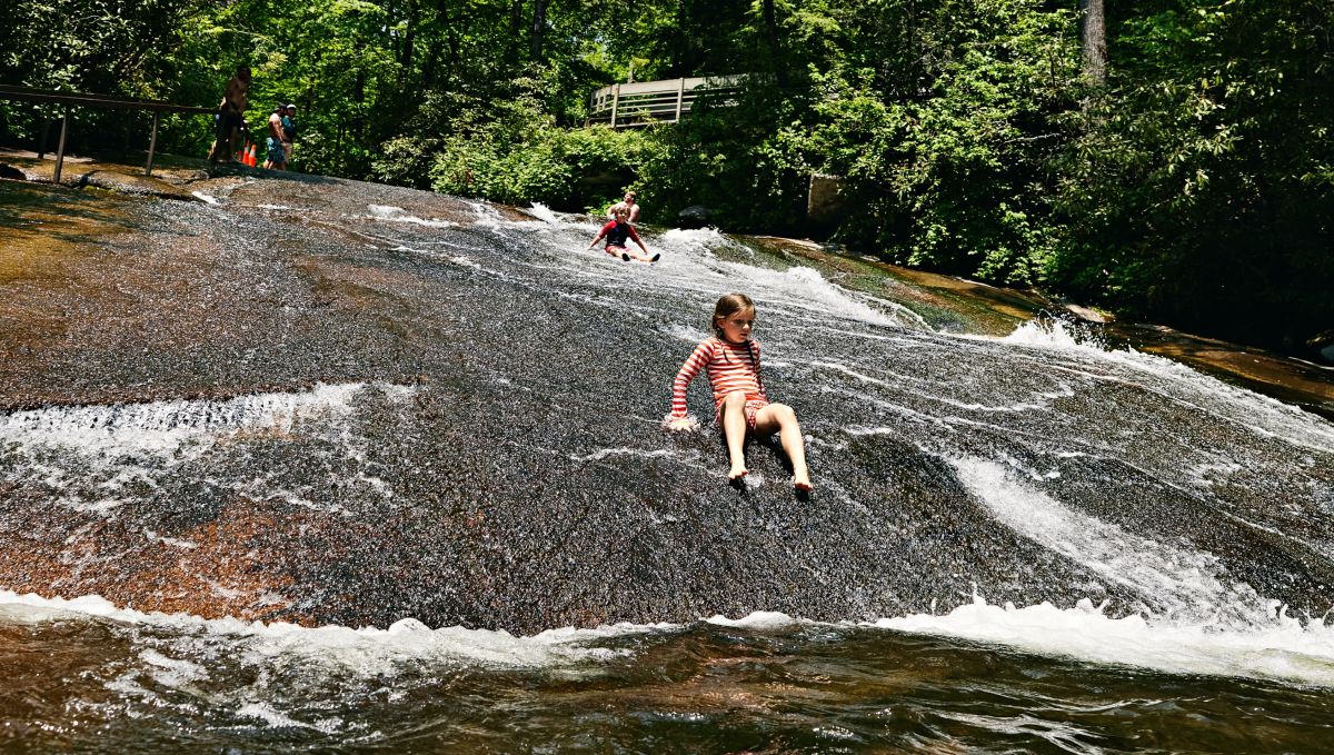 Children sliding down natural water slide with trees in background