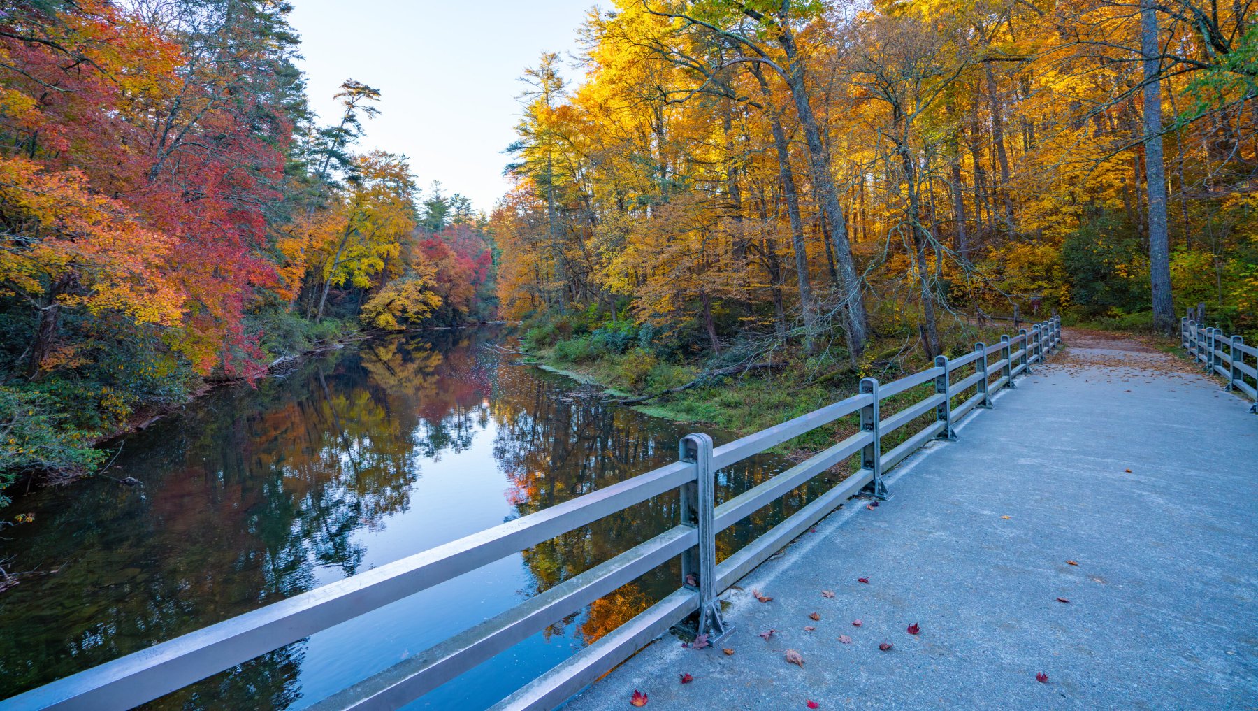 Calm Linville Falls Trail over river surrounded by brilliant fall foliage.