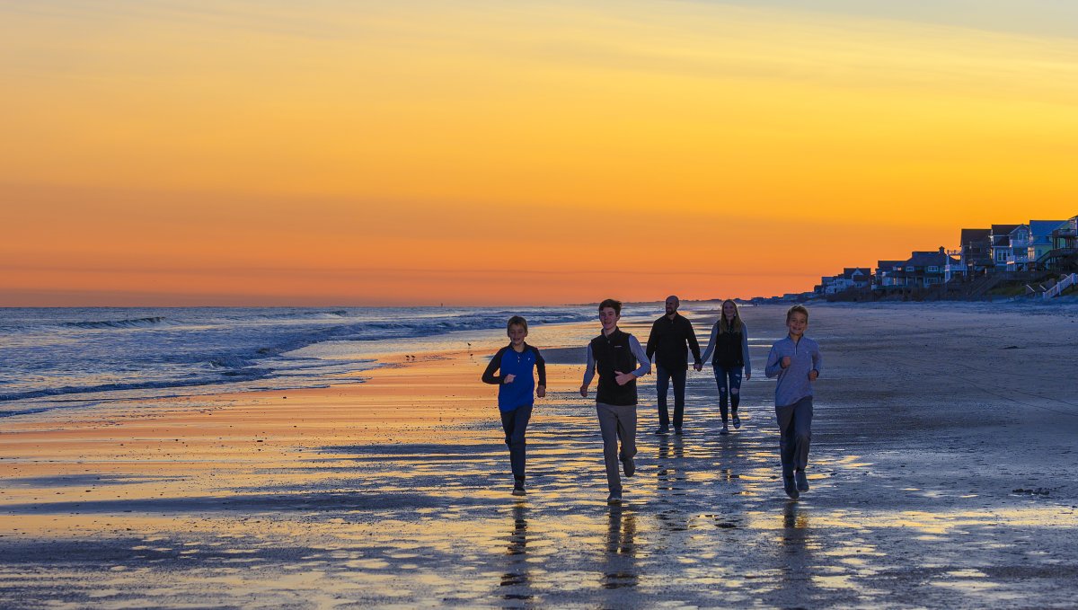 Family of 5 walking on the otherwise empty beach during bright orange and yellow sunset