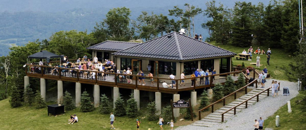 Aerial of 5506' Skybar with tons of people around grounds and on porch with mountains in distance.