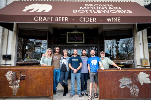 Friends posing for camera in front of Brown Mountain Bottleworks on outdoor patio under brown awning