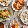 Various plates of seafood and mussles scatter the screen with wine glasses and silverware in between. 