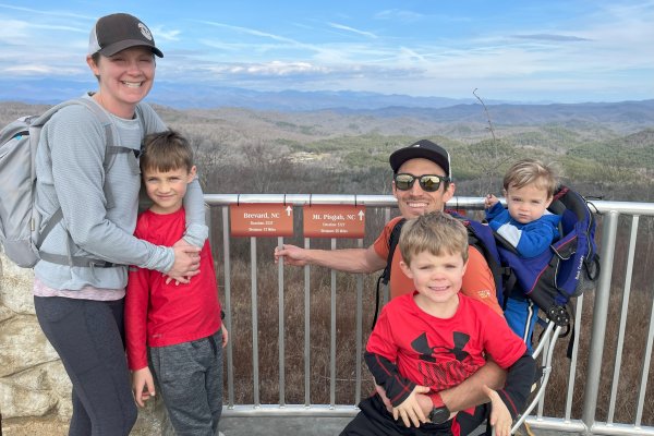 Family of 5 posing in front of blue mountains and green trees at overlook