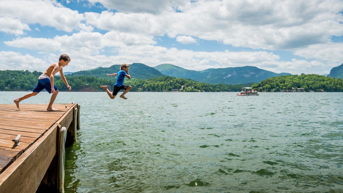 Two boys jumping off dock into Lake Lure with mountains in background during daytime