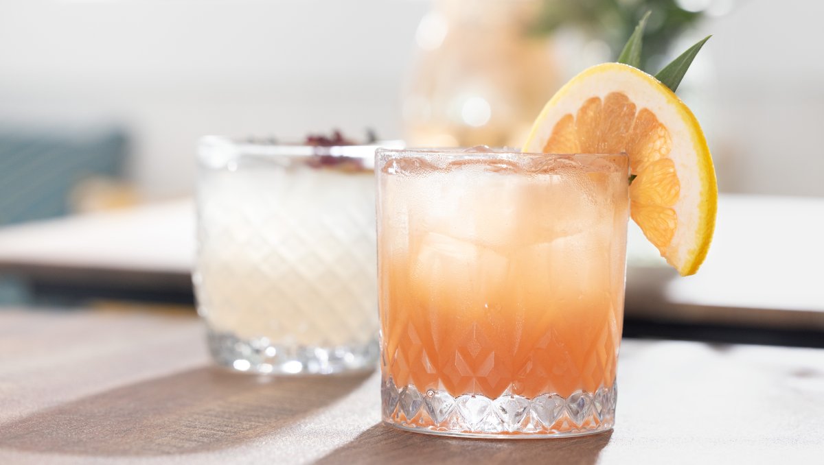 Closeup of two beautiful mocktails with fruit garnishes sitting on table.