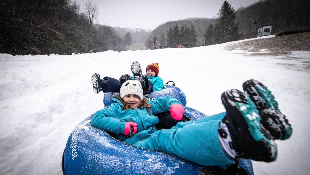 Two kids on snowtubes sliding down a snowy hill on gray day at Hawksnest Snow Tubing Park