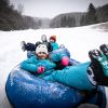 Two kids on snowtubes sliding down a snowy hill on gray day at Hawksnest Snow Tubing Park