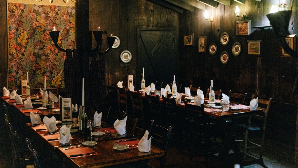 Interior of restaurant's dark dining with tables set and wall lamps lit