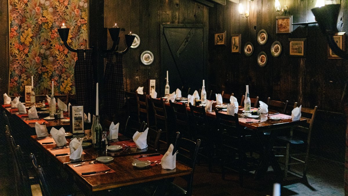 Interior of restaurant's dark dining with tables set and wall lamps lit