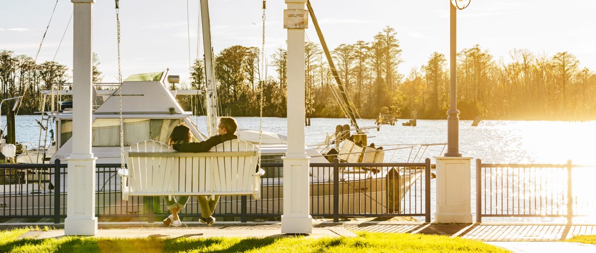 Couple swinging along waterfront in Downtown Washington with river and boat in background.