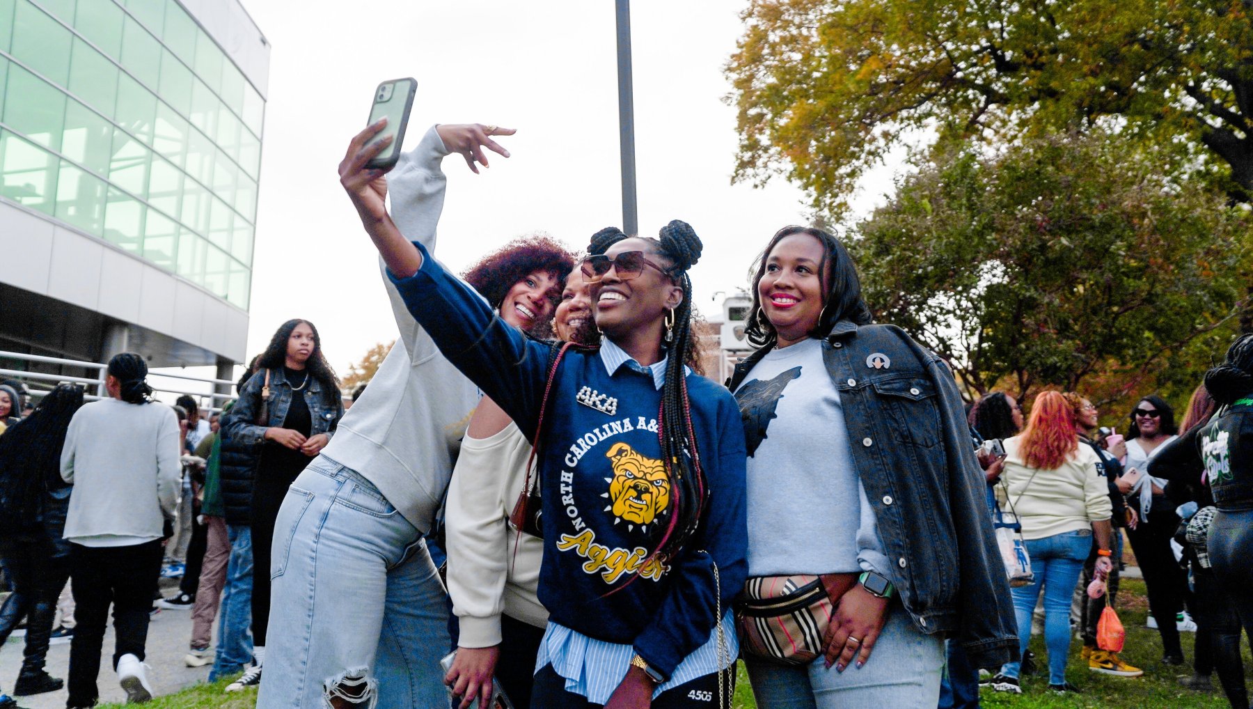 Friends taking selfie with more tailgaters behind them at NC A&T Homecoming.