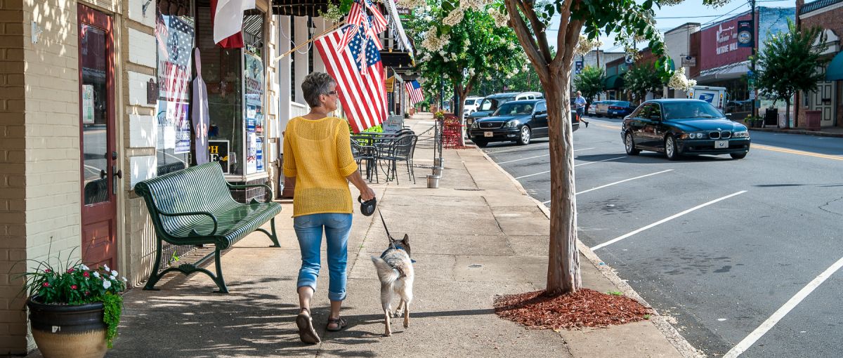 Woman walking her dog down on sidewalk in downtown Rutherford on sunny day