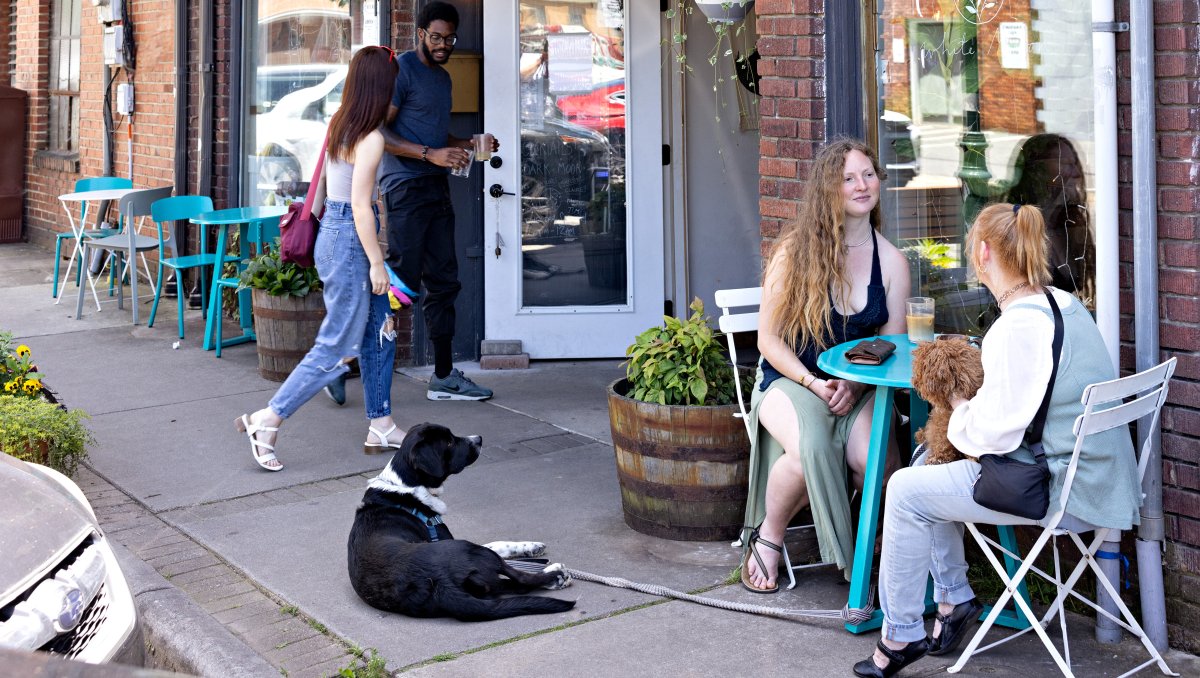 Friends enjoying coffee on patio as another customer walks into brick coffee shop.