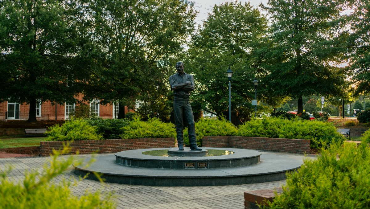 Dale Earnhardt statue in Dale Earnhardt Plaza surrounded by brick plant holders, bushes and trees in background during daytime