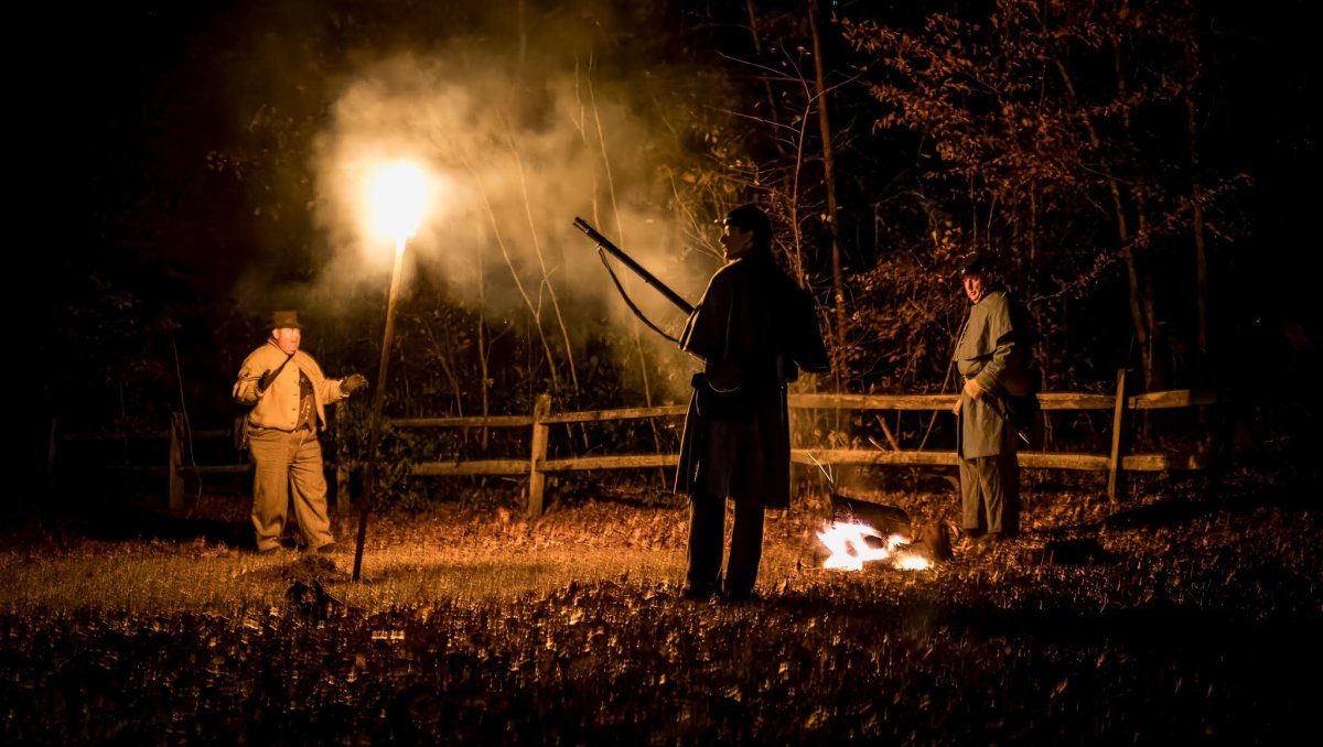 Civil War re-enactors standing around a fire at night.