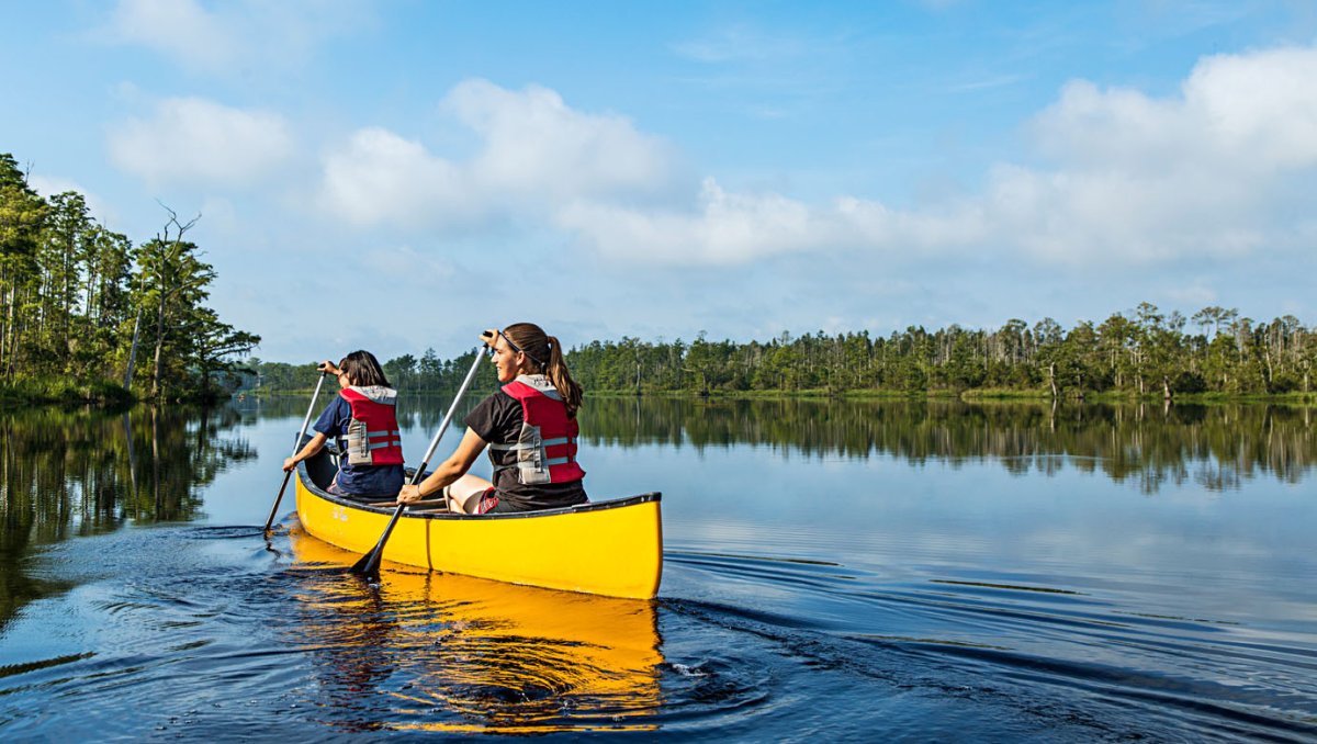 Two friends paddling in yellow canoe through calm river with green trees in distance on shoreline