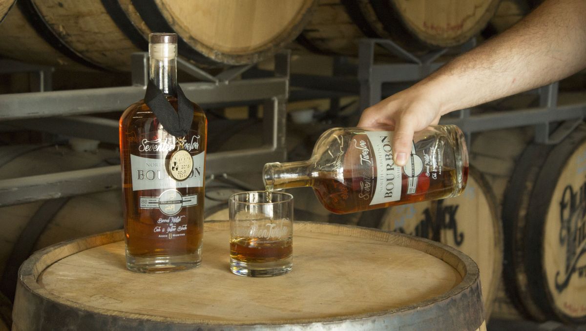 Seventeen Twelve Spirits bourbon being poured into glass with barrels in background
