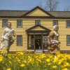 Two children dressed in 1700s period garb running in field of yellow flowers in front of historic building