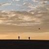 Silhouettes of two people flying a kite on sand dune, orange sky in background