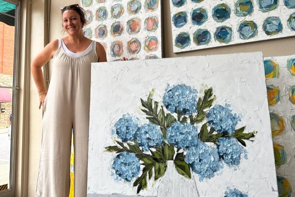 Woman stands next to large floral art with art on wall behind her