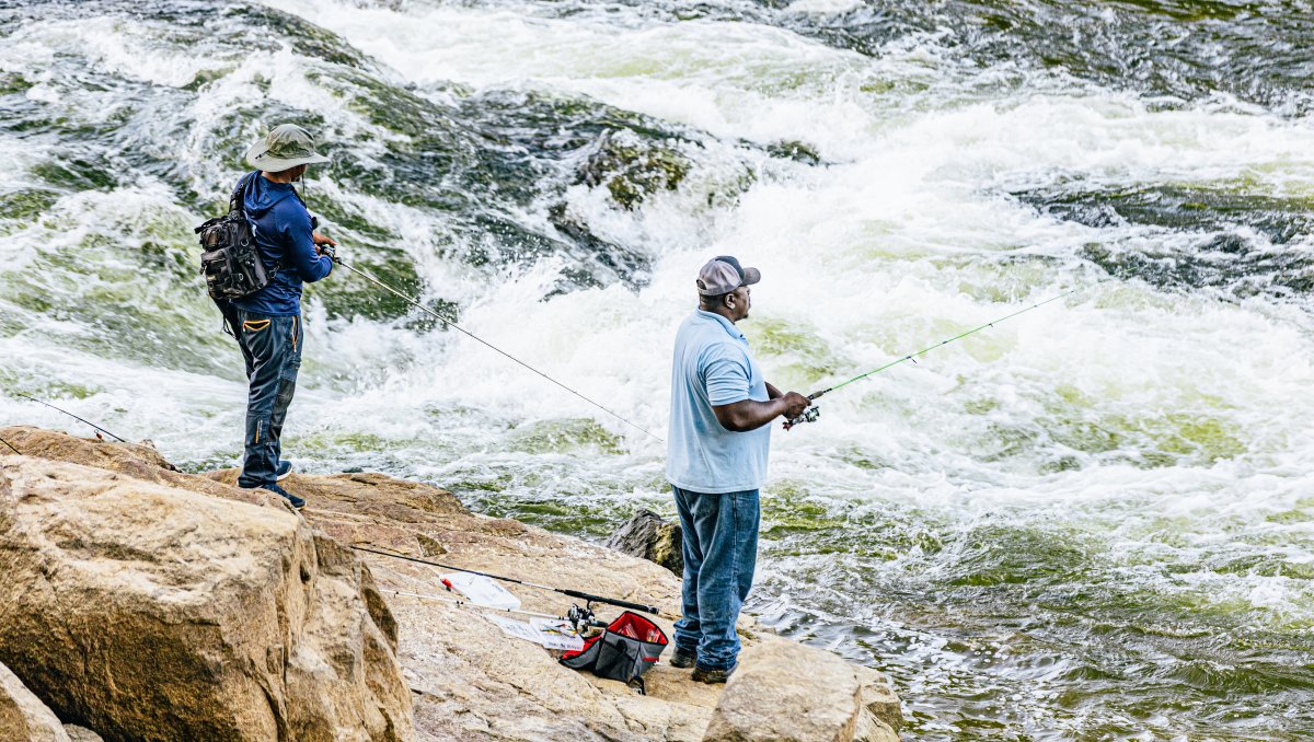 Two men fishing from rocks into raging river.