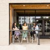 Three smiling friends drinking wine on front patio of wine store during daytime.