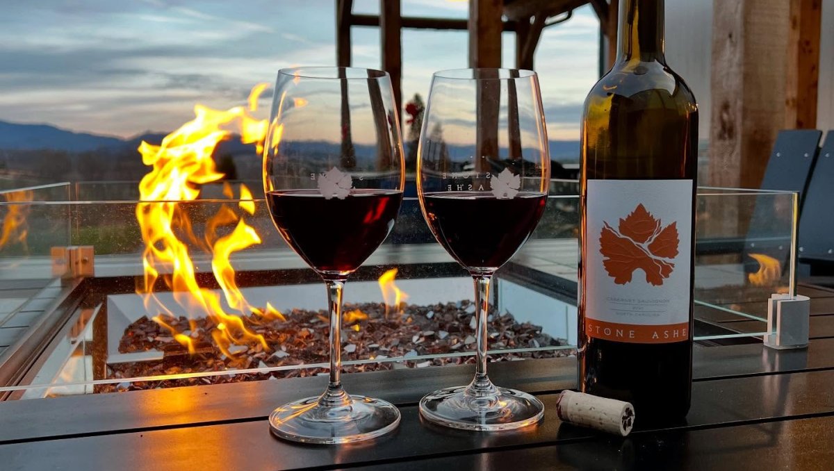 Bottle of wine and two glasses of wine sitting on firepit at winery with mountains in background.