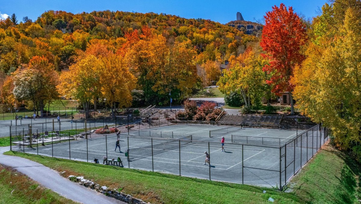 People playing tennis on courts with mountains and fall foliage in background
