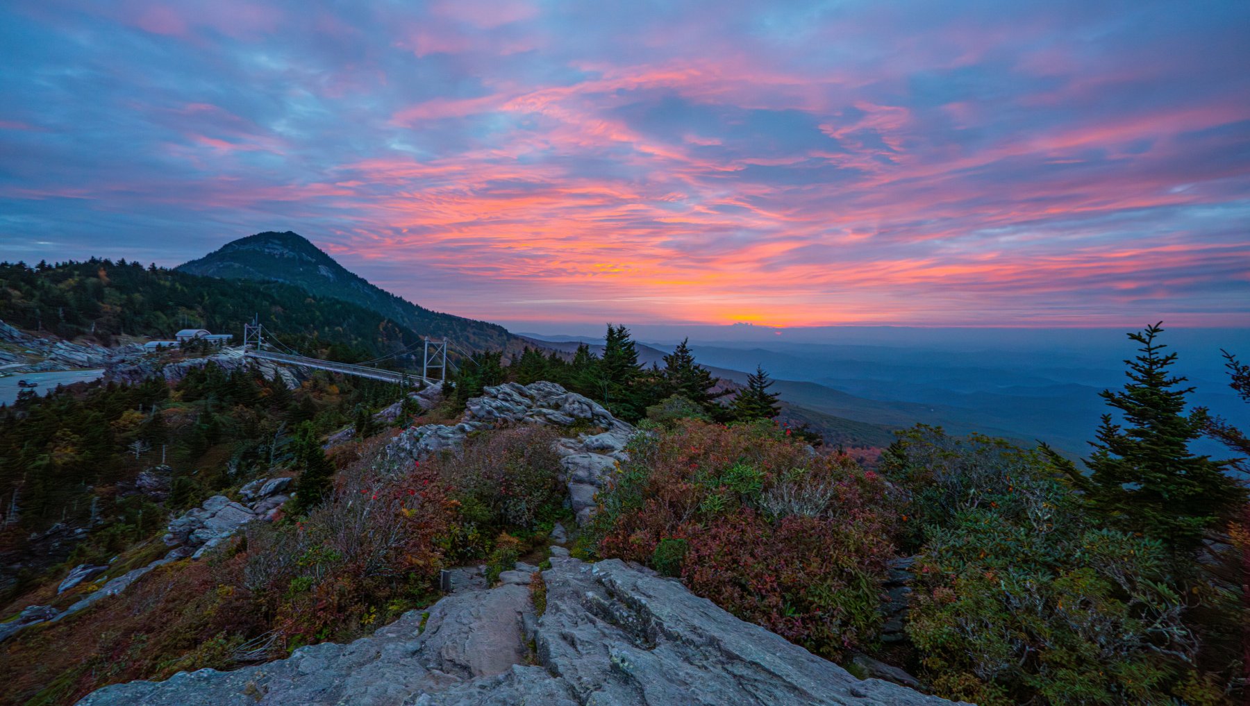 Aerial of Mile High Swinging Bridge on Grandfather Mountain during fall under brilliant pink sunset.