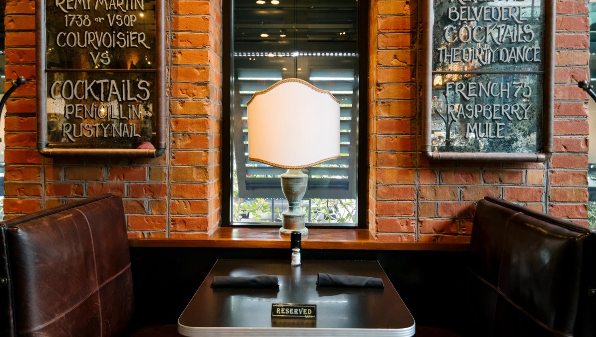 Dark, cozy restaurant booth with vintage drink signs on brick wall
