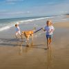 Two children running with golden retriever on beach in Corolla during sunny day