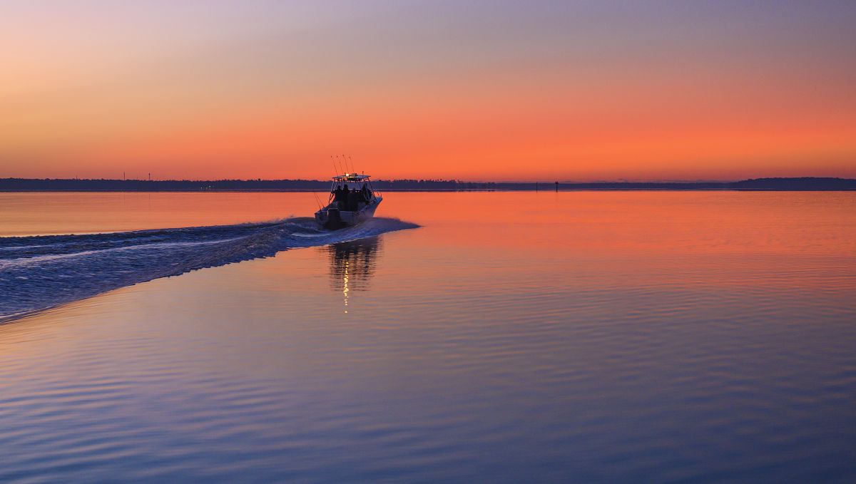 Fishing charter sailing into the distance on calm water during a bright orange sunrise