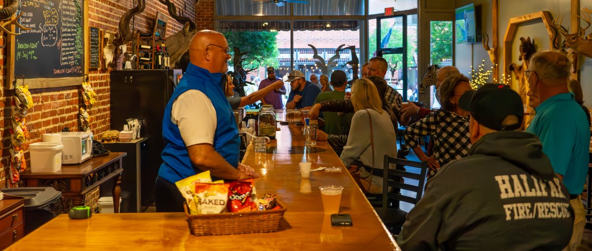 People sitting at bar enjoying drinks with smiling bartender exposed brick behind bar