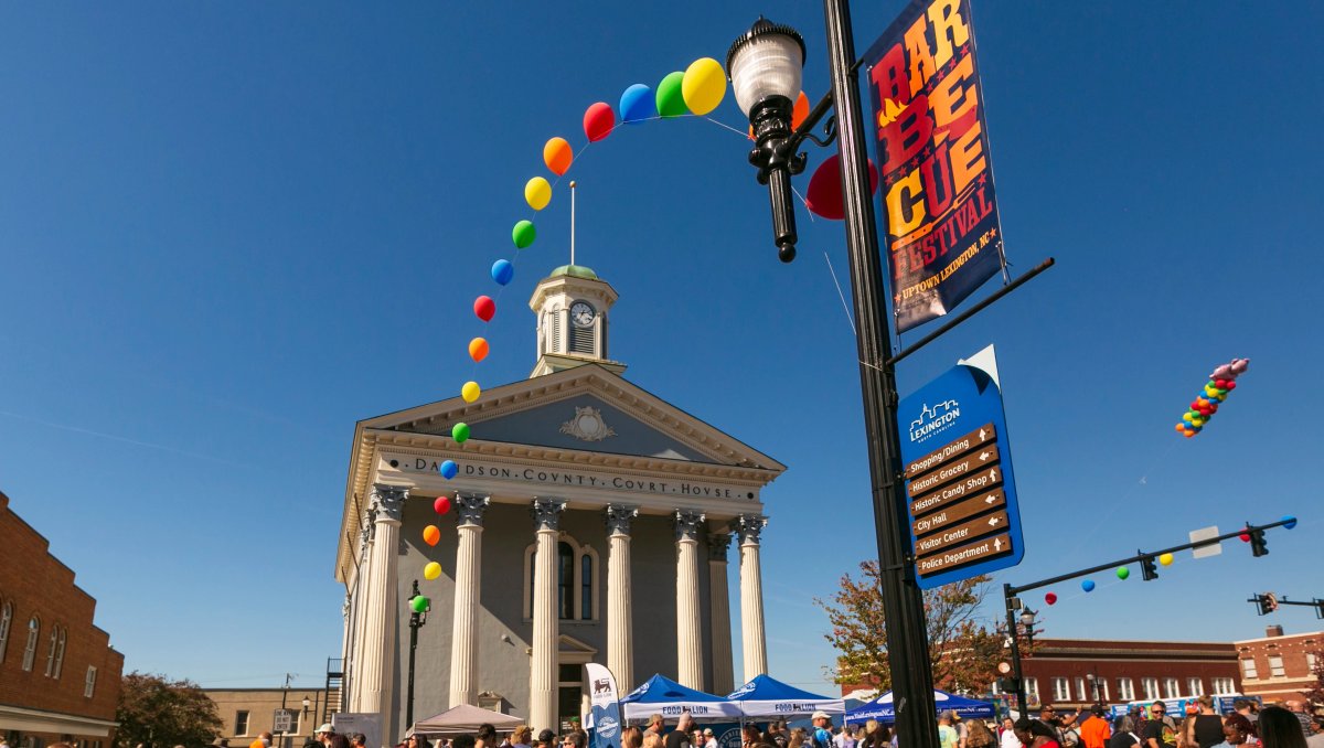 People enjoying festival in front of a courthouse with balloons and BBQ festival signage on light post