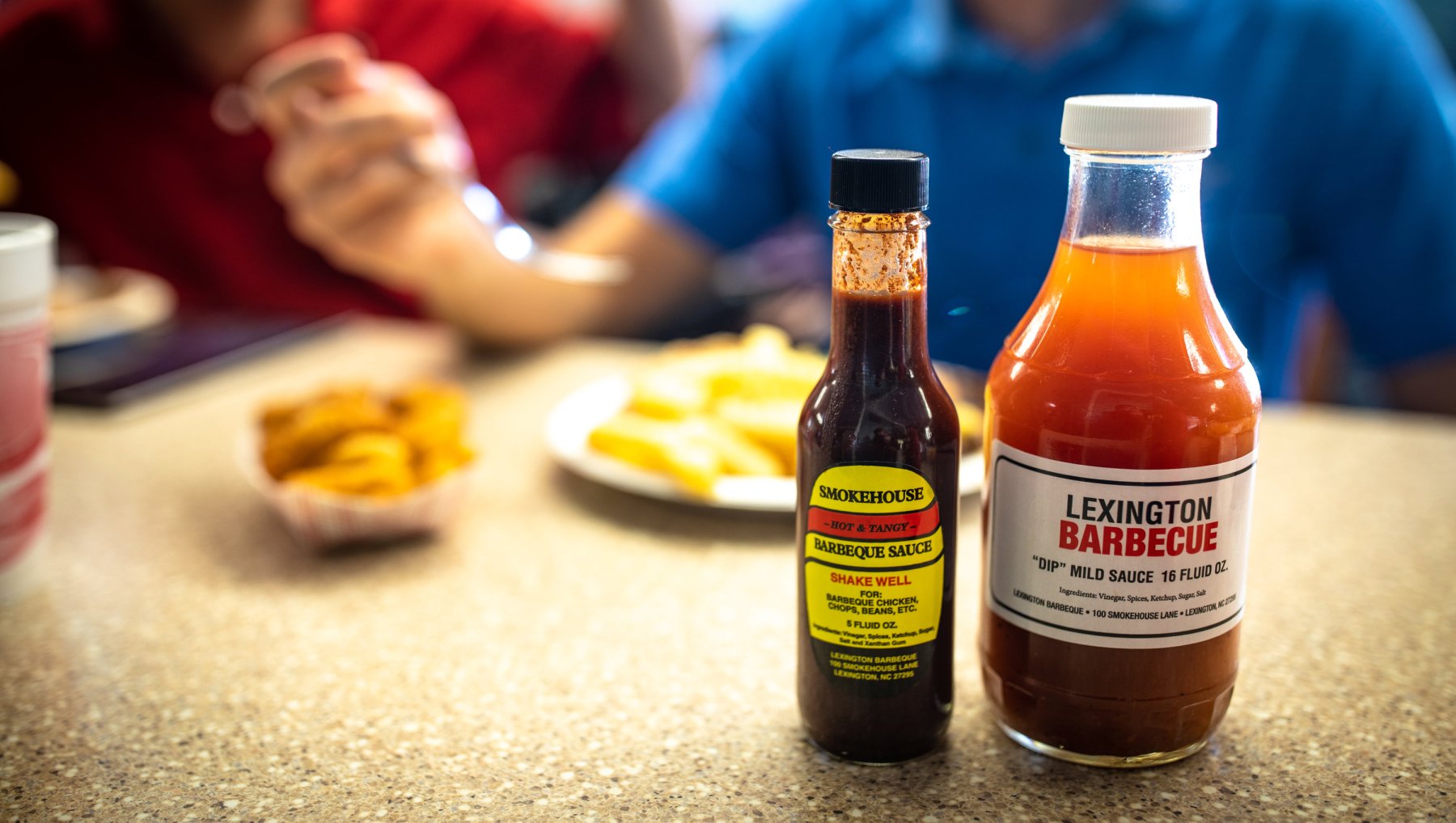 Lexington Barbecue sauces in foreground on counter as people eat plate of food in background.