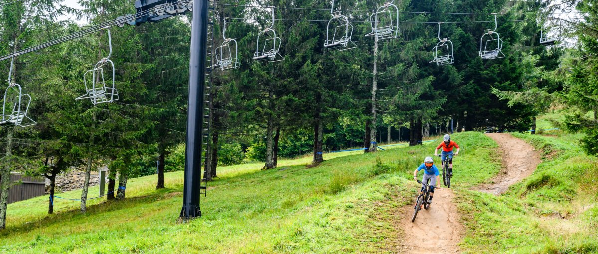 Two friends riding biking through Beech Mountain during summer with ski lifts above them