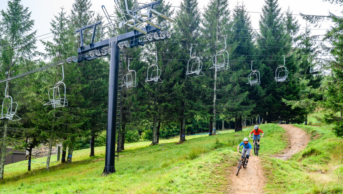 Two friends riding biking through Beech Mountain during summer with ski lifts above them