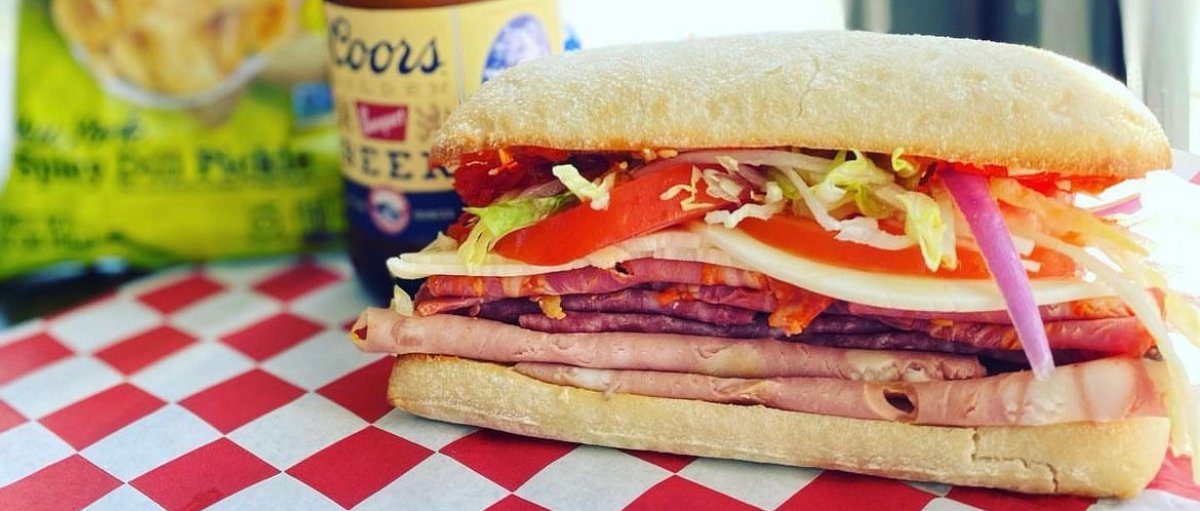 Close-up of deli sandwich, bottle of beer and bag of chips sitting on table