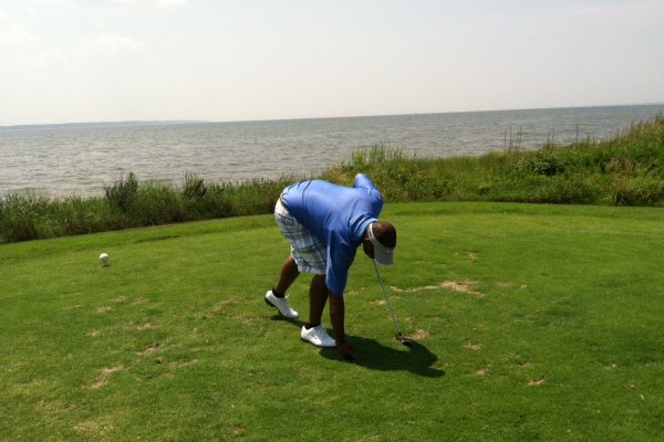 Man reaching into hole to pick up golf ball with ocean in background