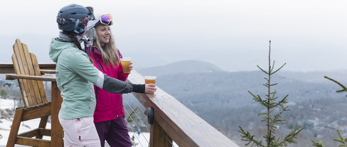 Two friends drinking beers on bar deck overlooking mountains and ski slopes
